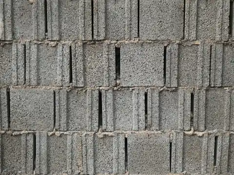 A wall of gray concrete blocks with rough mortar joints and narrow gaps between some of the blocks
